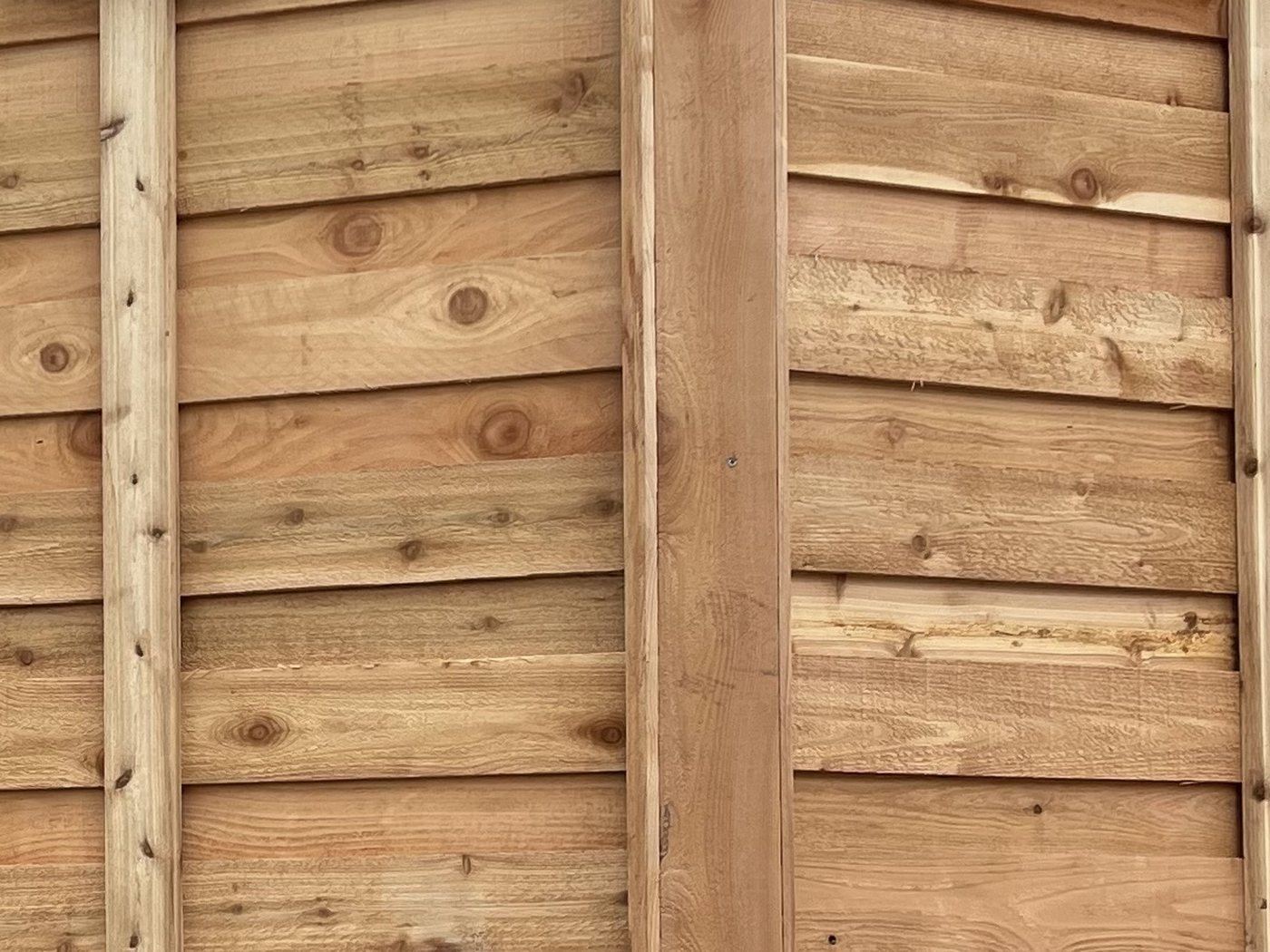 Close view of a cedar fence where each board overlaps the one below it, beside a post boxed in cedar