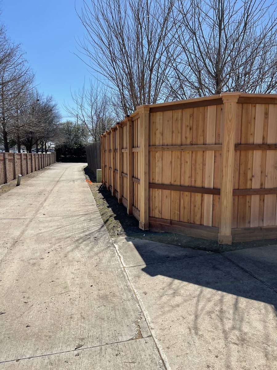 New cedar board-on-board fence with top cap and stone base along a North Dallas sidewalk