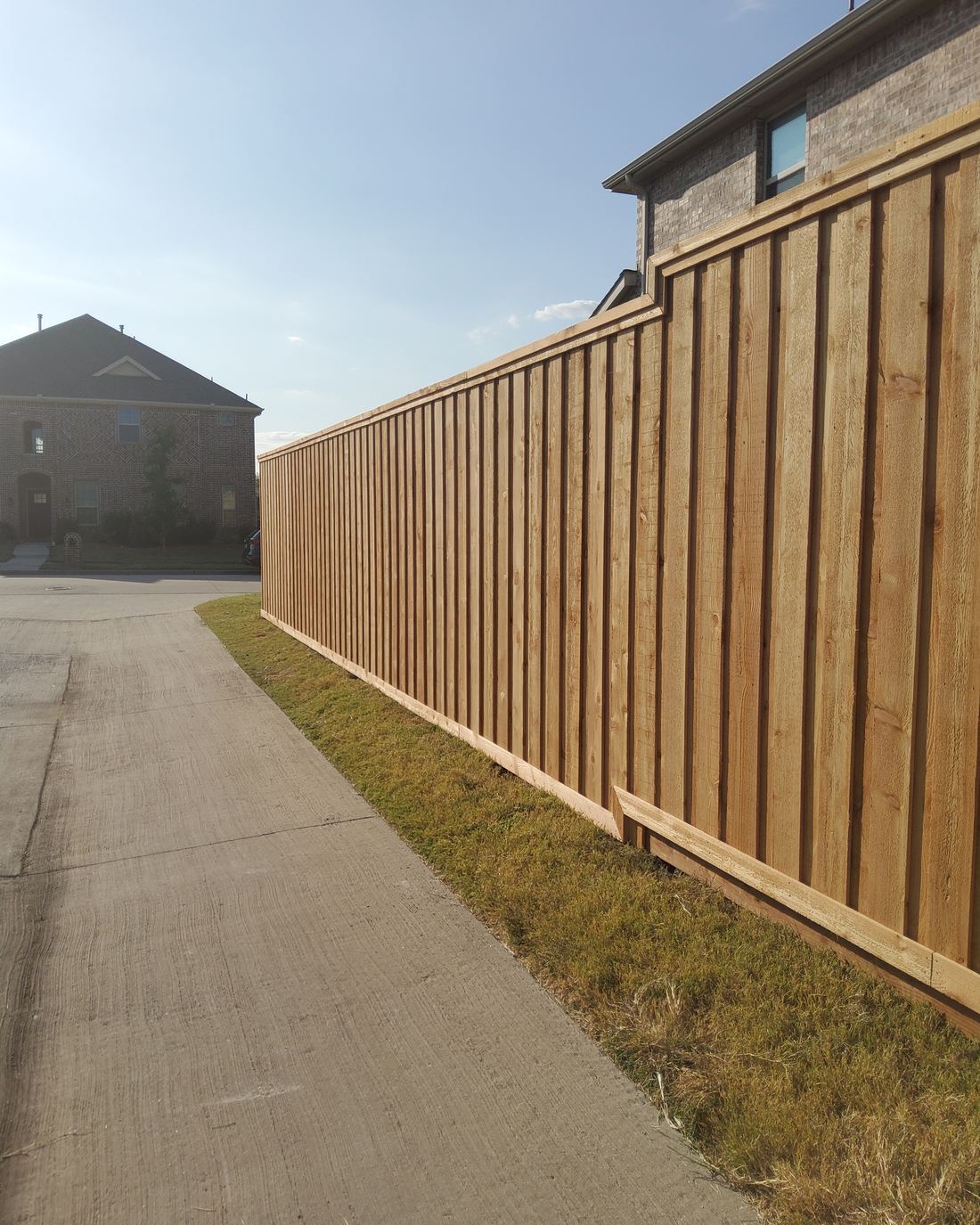 A new cedar board-on-board privacy fence with cap and trim running along a sidewalk