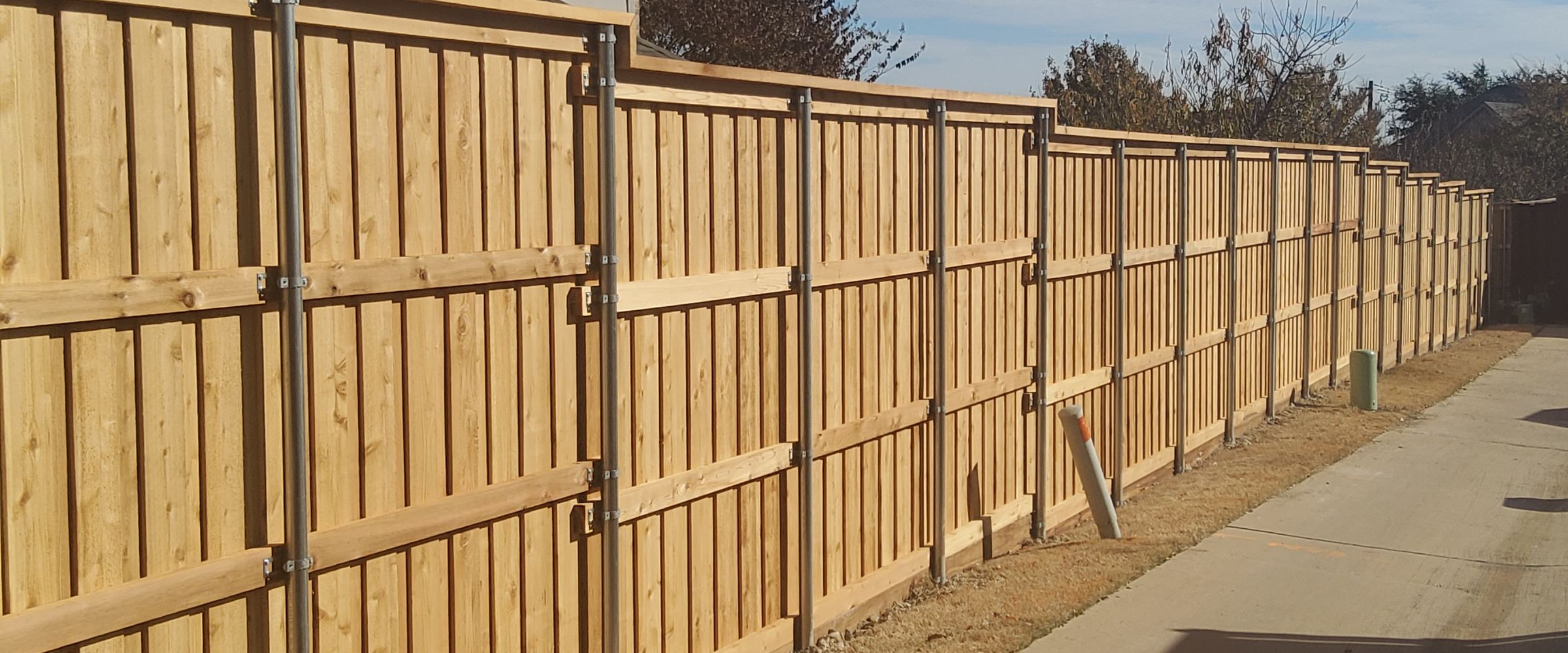 A cedar fence mid-build: posts and rails set along an alley, boards going on
