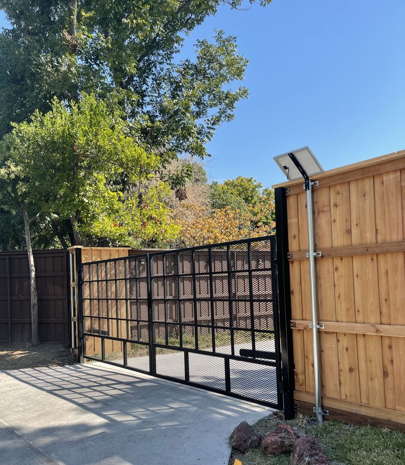 A black steel gate hung on a galvanized post beside a cedar fence, a drive running through