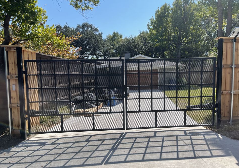 Black steel double estate gates closed across a driveway, cedar fence on either side