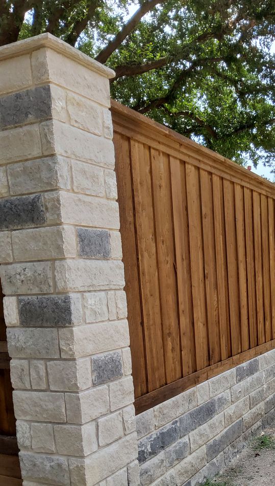 Cedar fence panels between a cut stone column and a stone base wall, under a maple in fall color