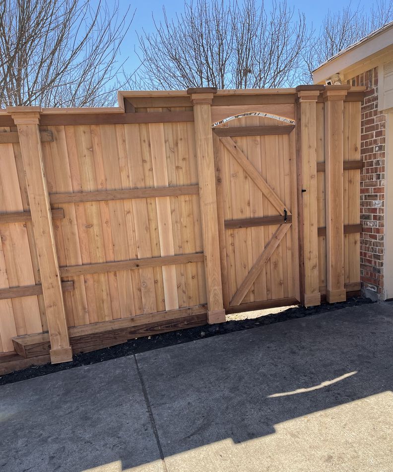 Cedar fence meeting a brick house wall, with a braced walk gate and a stepped top rail