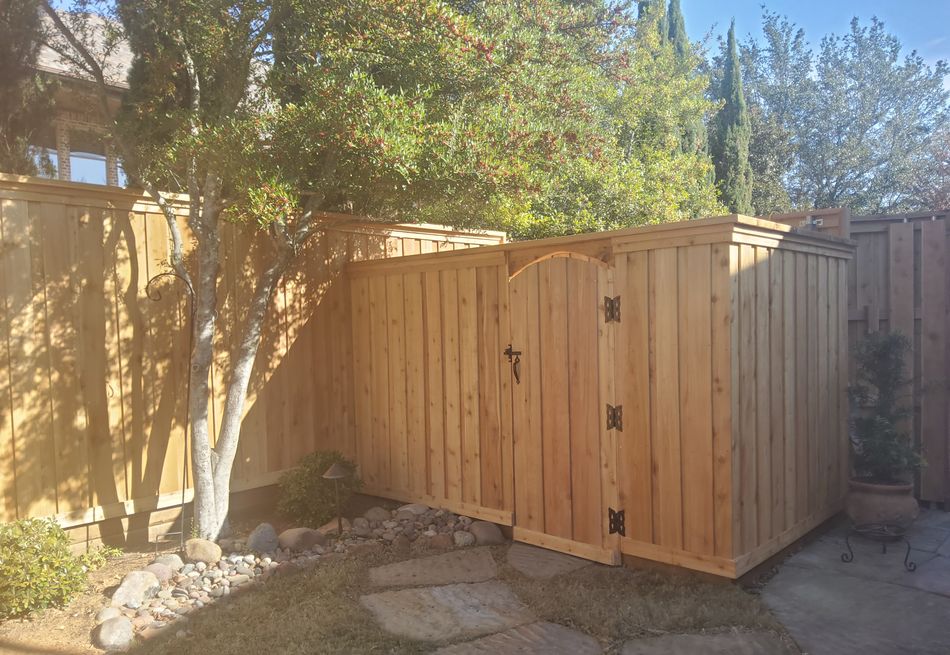 Cedar fence and arched gate at the back of a yard, flagstone underfoot and a shade tree above