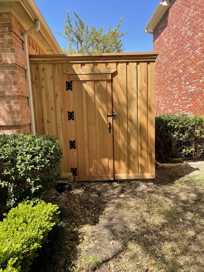 A cedar walk gate with black strap hinges set between two brick walls, boxwood on either side
