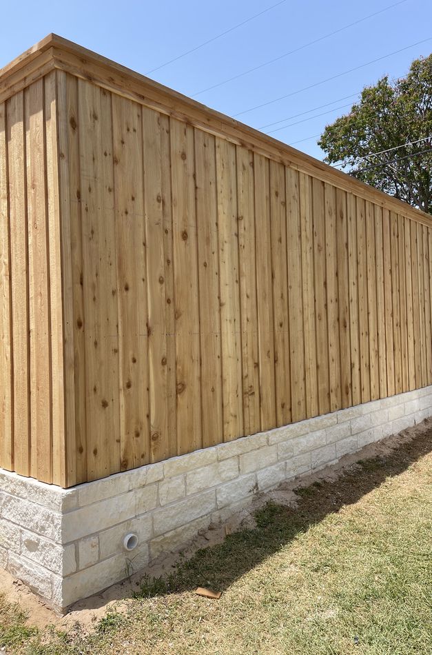 A tall cedar board-on-board fence on a white limestone base running down a Texas back lot line