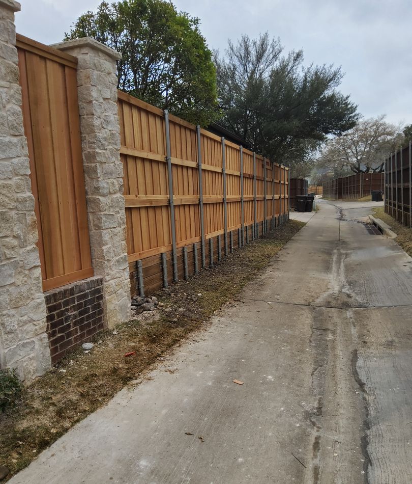 Cedar fence panels set between cut stone columns, running the length of a back alley