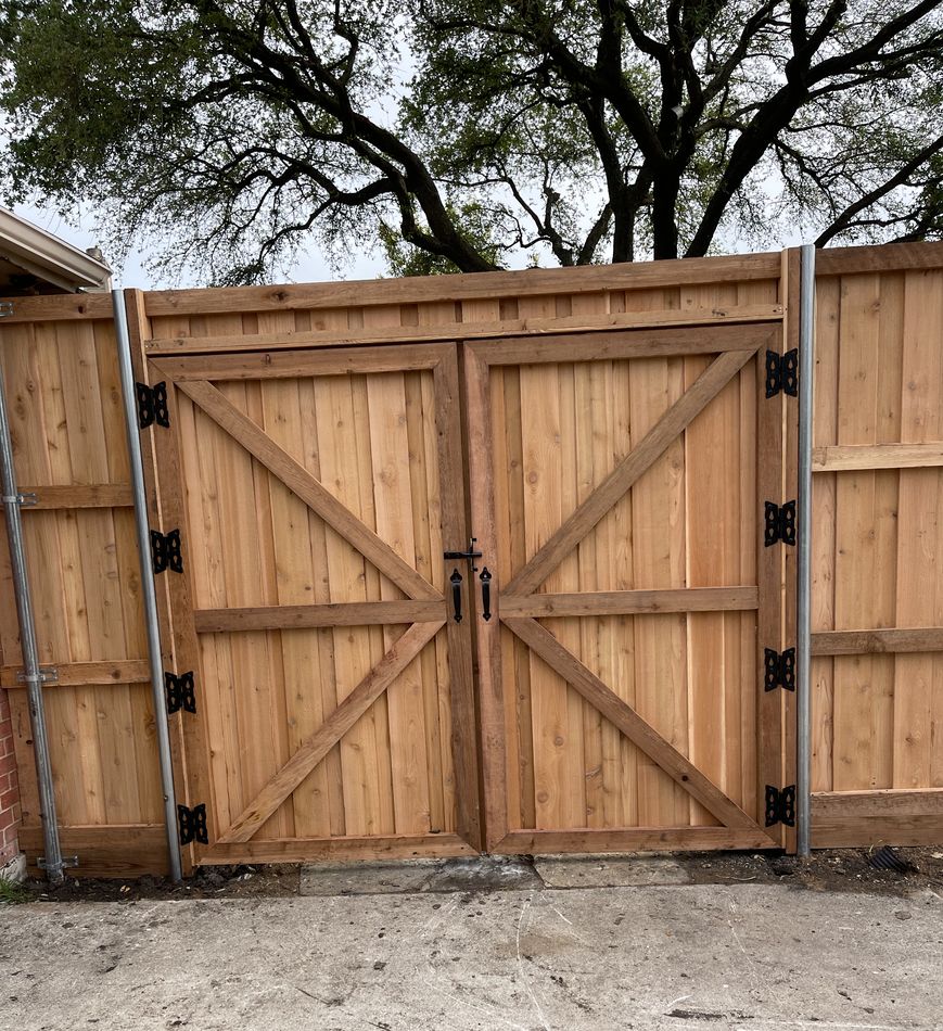Double barn-style cedar gates with cross bracing and black strap hinges across a drive