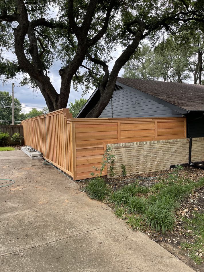 A horizontal-board cedar fence and gate wrapping the corner of a drive under a live oak