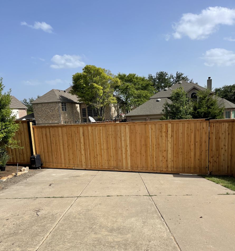 A full-width cedar slide gate closed across a wide concrete drive