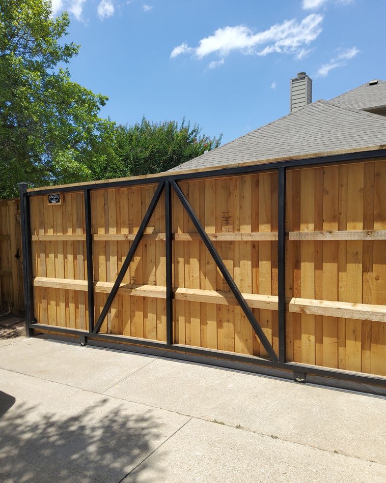 A cedar driveway gate built into a black steel frame, closed across a concrete drive