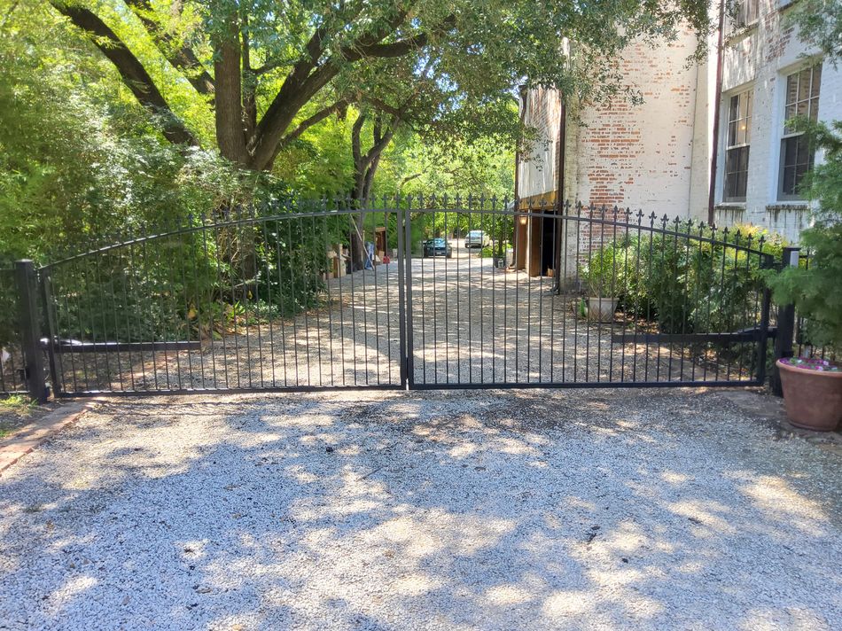 Black iron double estate gates closed across a gravel drive under an oak canopy
