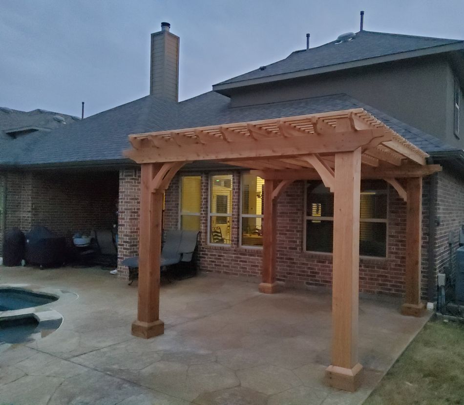 A cedar patio cover attached to the back of a two-story brick house at dusk