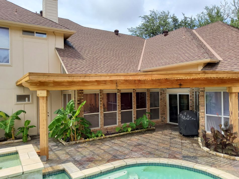 A cedar patio cover seen wide, brick paving and planting between it and the pool