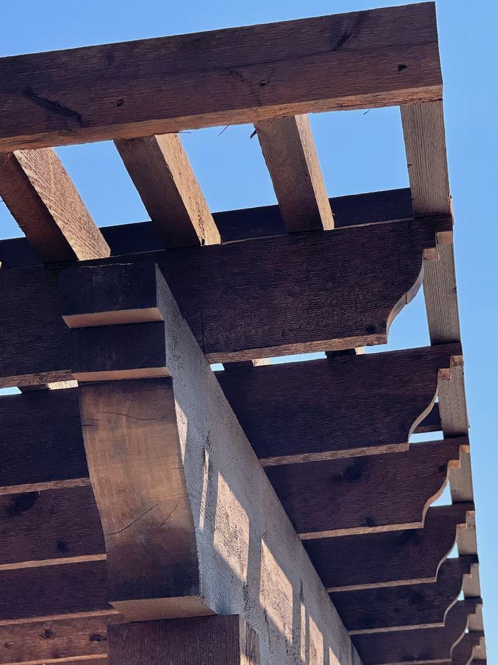 Stained cedar pergola rafters and corbels against a clear sky