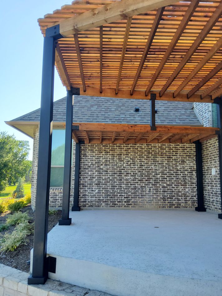 A cedar slat pergola on black steel posts against a stone house