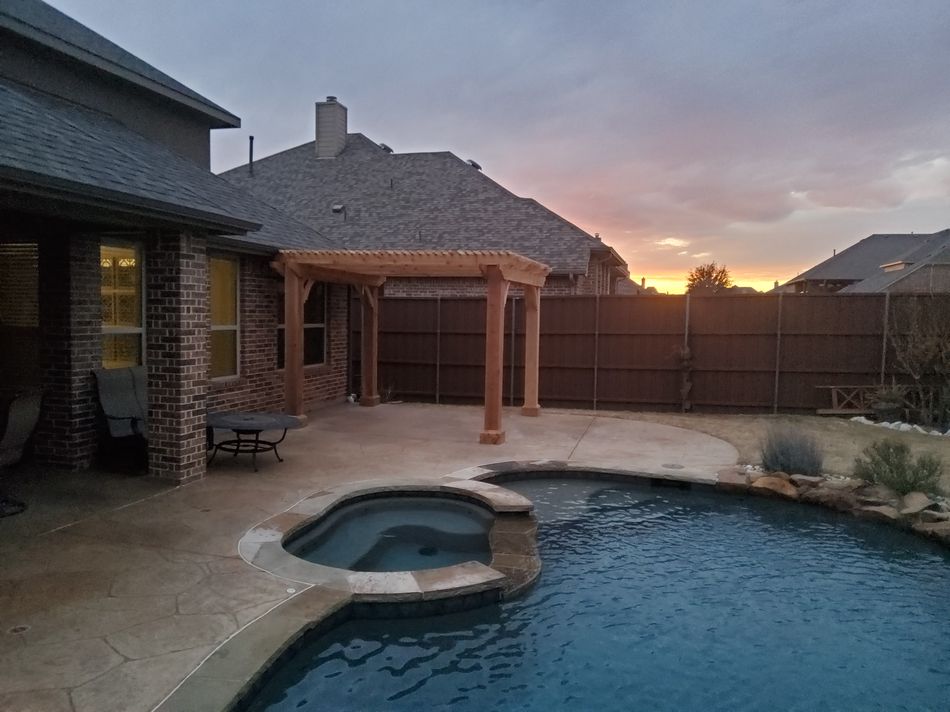 A cedar pergola off the back of a brick house at sunset, pool and spa in the foreground