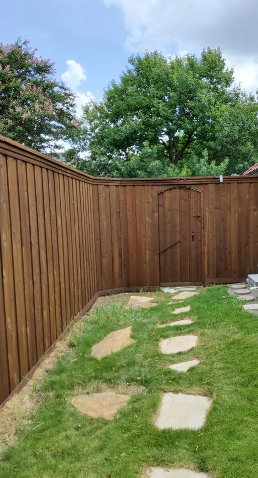 A stained cedar fence turning a corner with an arched gate, flagstone path across the lawn