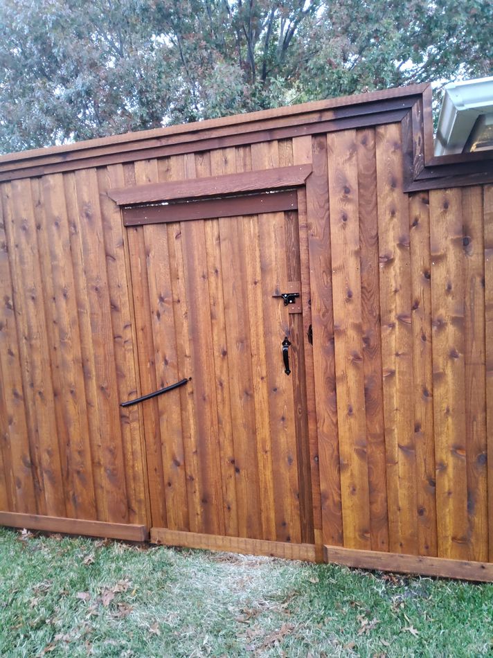 A stained cedar gate framed into a stained fence run, deep brown against frosted grass