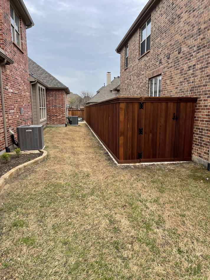 A stained cedar fence running down a side yard between two brick houses