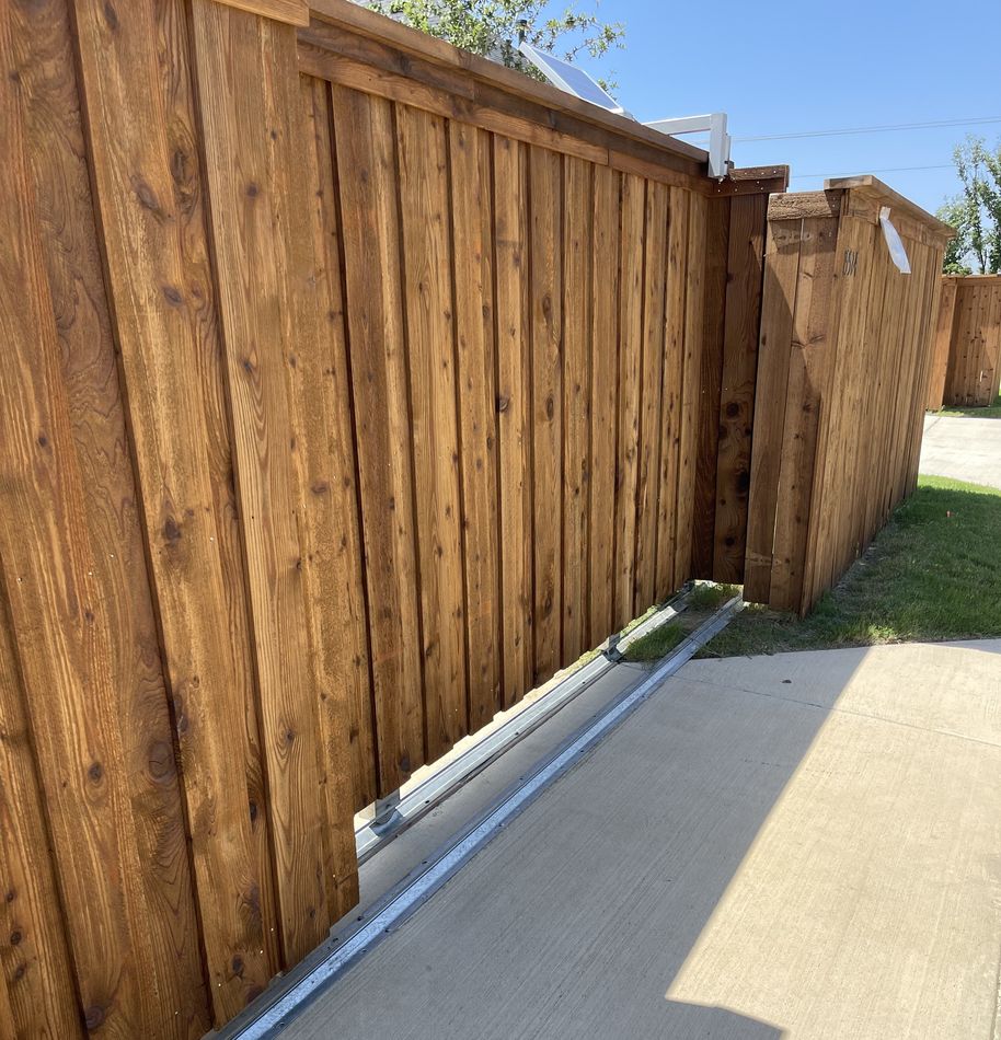 A stained cedar slide gate standing on its track along a concrete drive