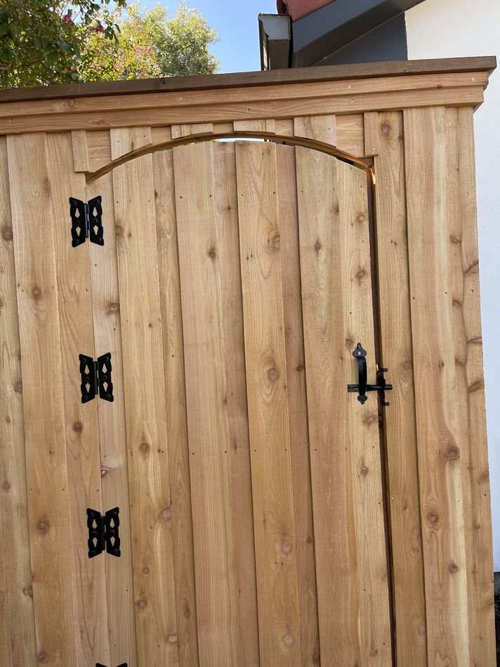 An arched-top cedar walk gate with black strap hinges and a thumb latch, seen close up