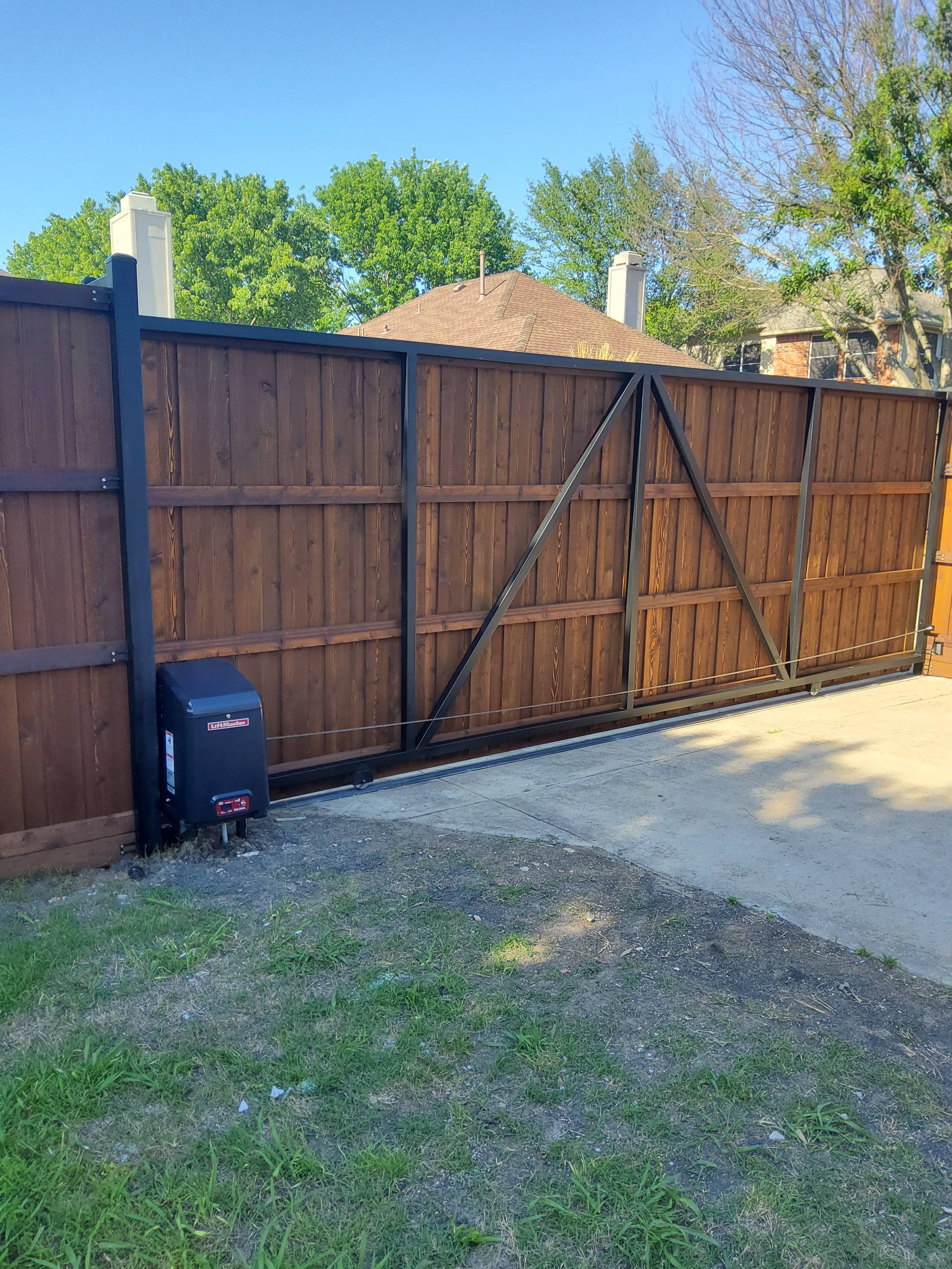A dark-stained cantilever sliding gate on black steel with its automatic opener in frame