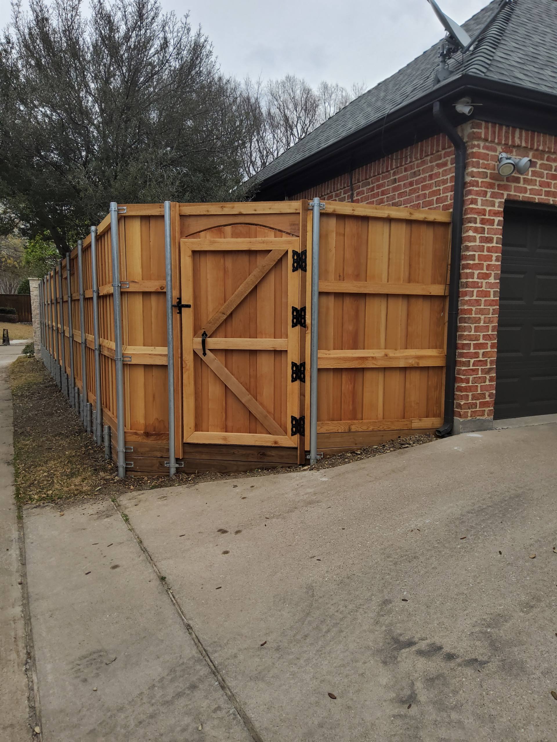 An arched cedar driveway gate with black iron hinges beside a brick garage