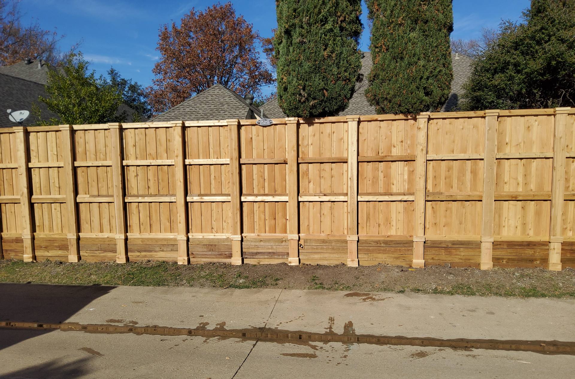 A new cedar board-on-board fence line running down a sunlit North Dallas street