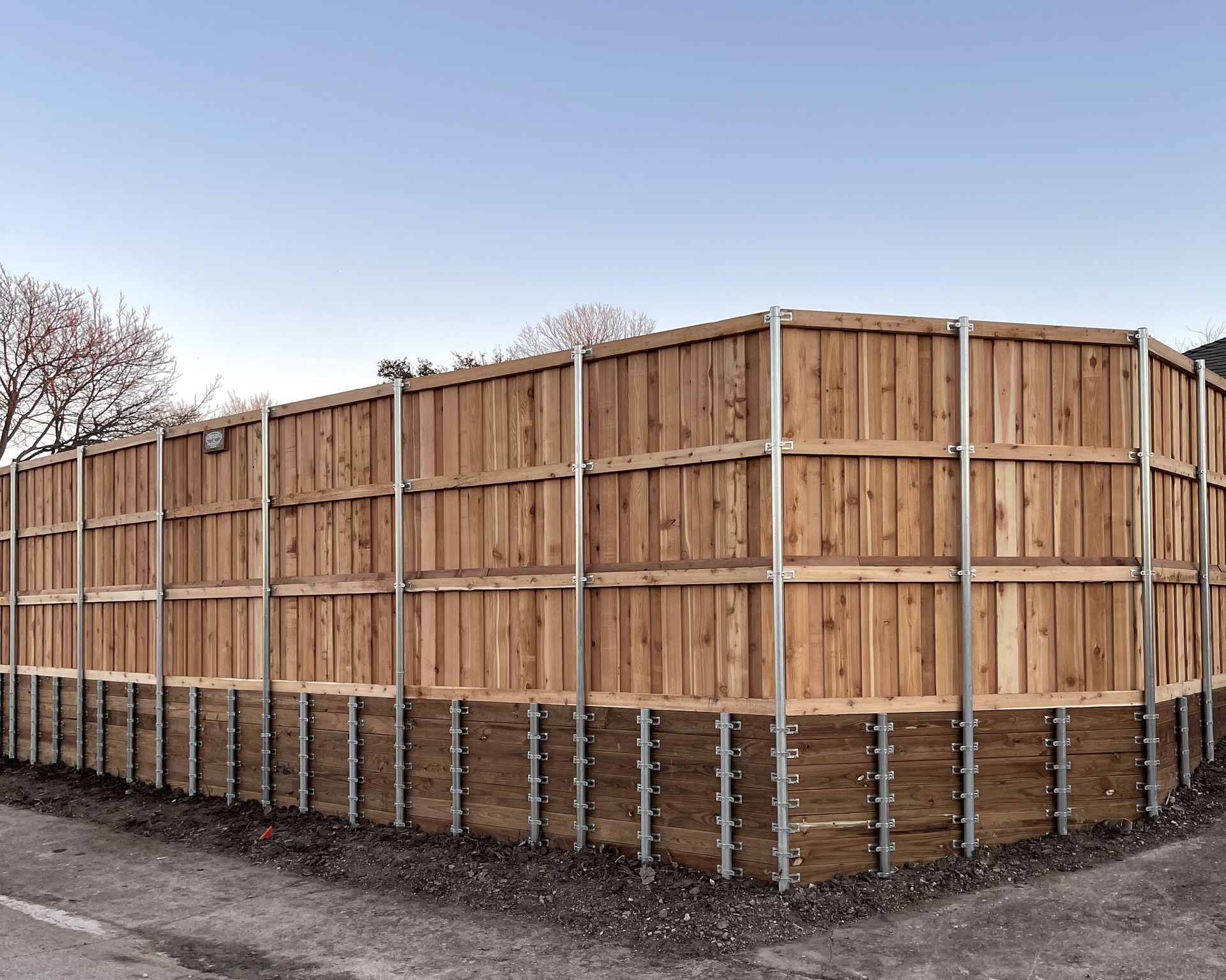 A long board-on-board cedar fence corner under a wide morning sky in McKinney, Texas