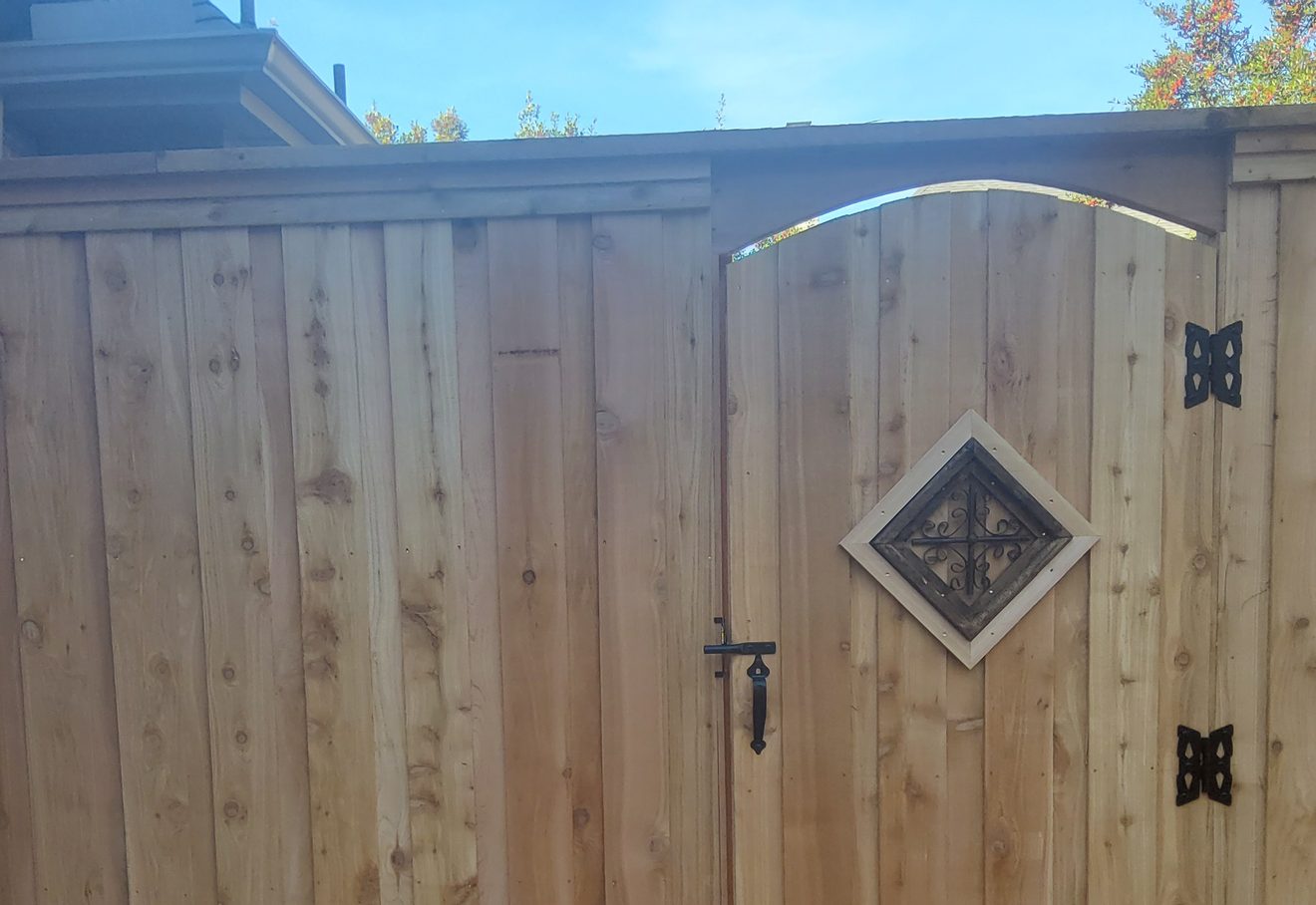 A cedar gate with an arched top and a diamond iron-scroll ornament, matched into the fence line
