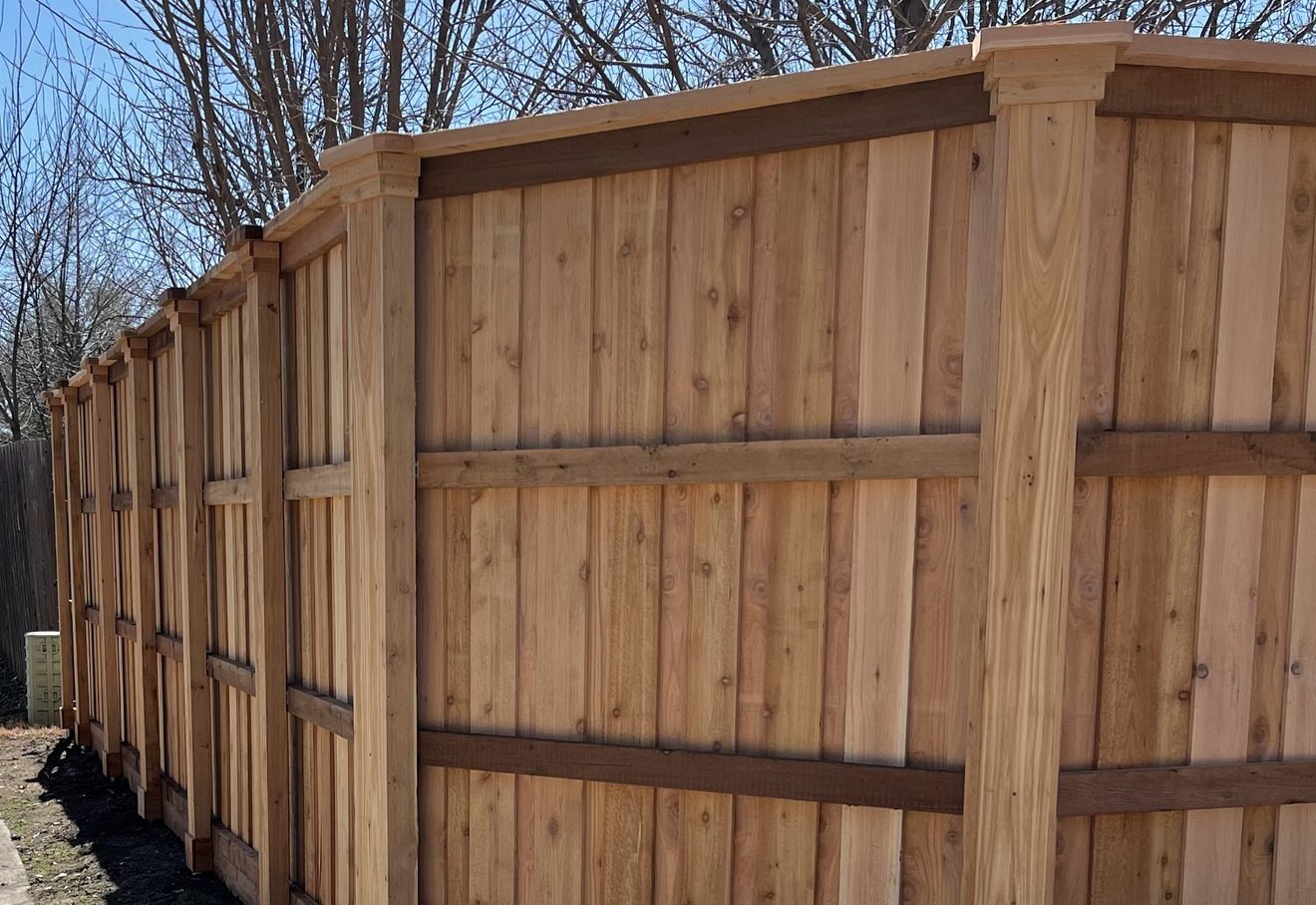 A new cedar board-on-board fence corner with cap-and-trim posts under a bright blue sky
