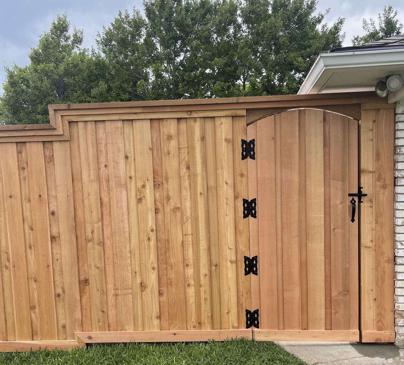 A clean board-on-board cedar fence and arched gate with black hinges beside a white brick McKinney home