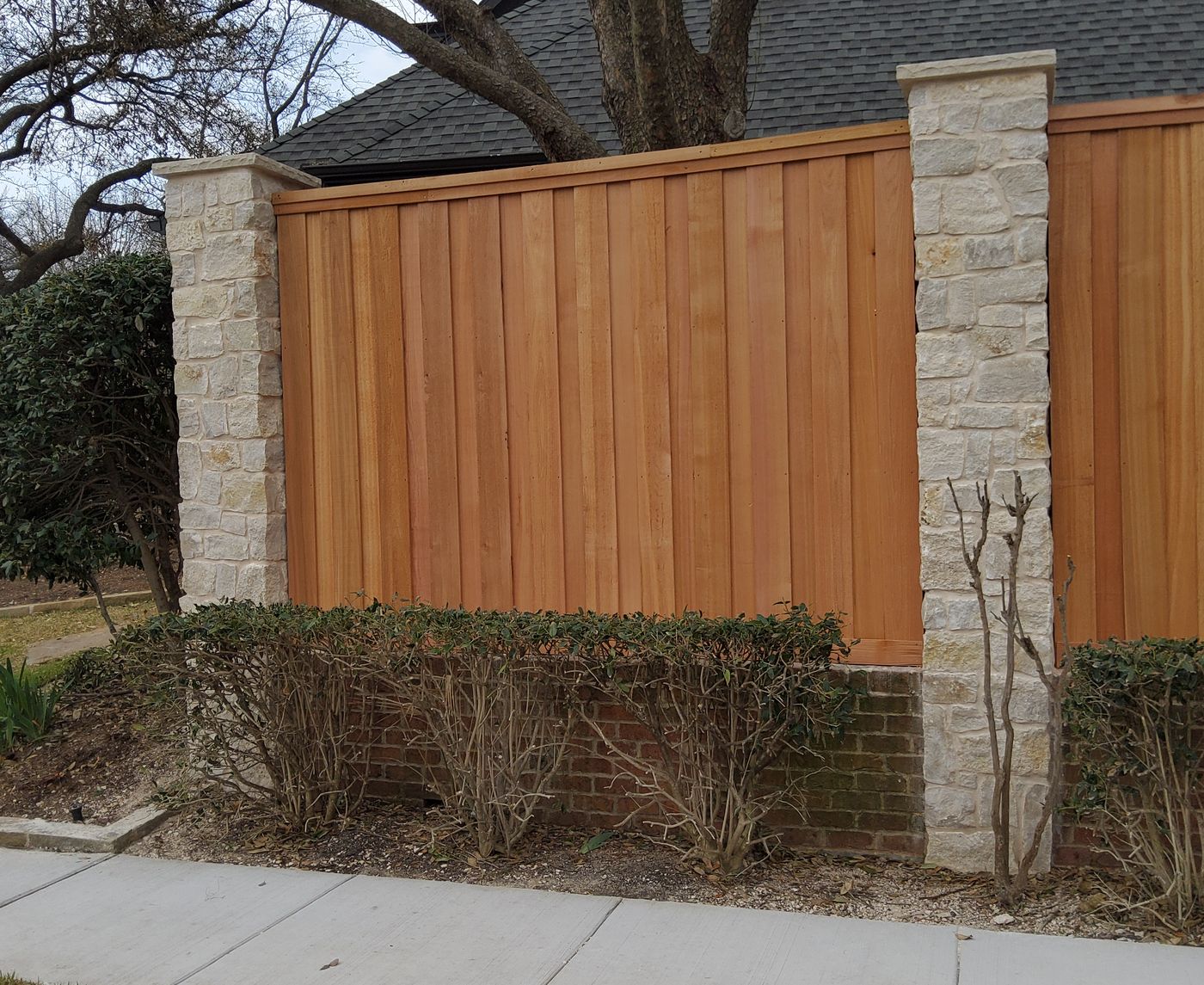 Cedar fence panels between cream stone columns in front of a large Plano home