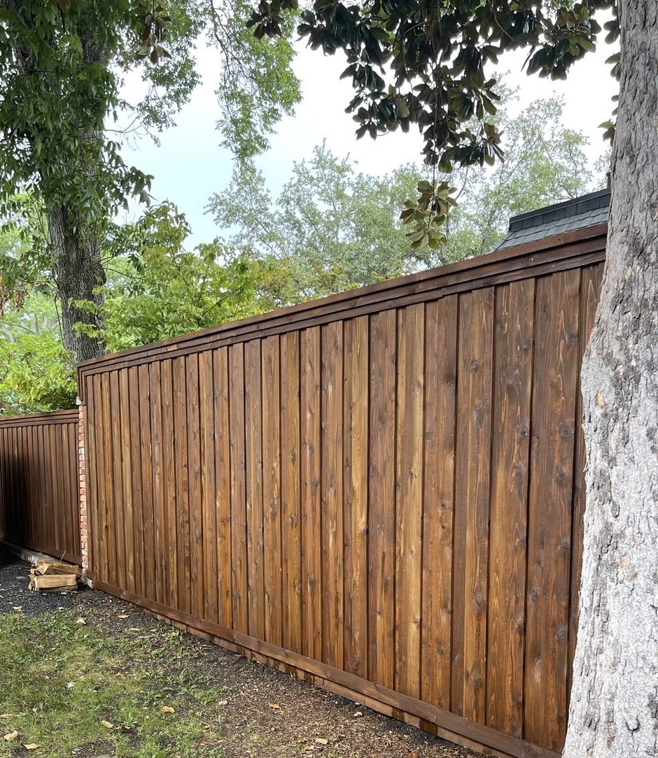 A freshly stained deep-brown cap-and-trim fence in North Dallas