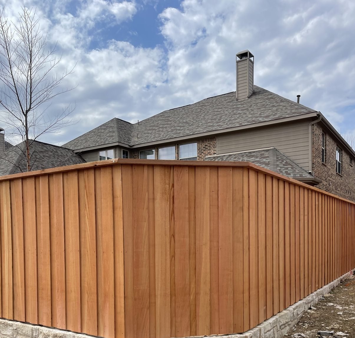 A tall Future Fence board-on-board cedar fence with trim caps built on a stone retaining wall