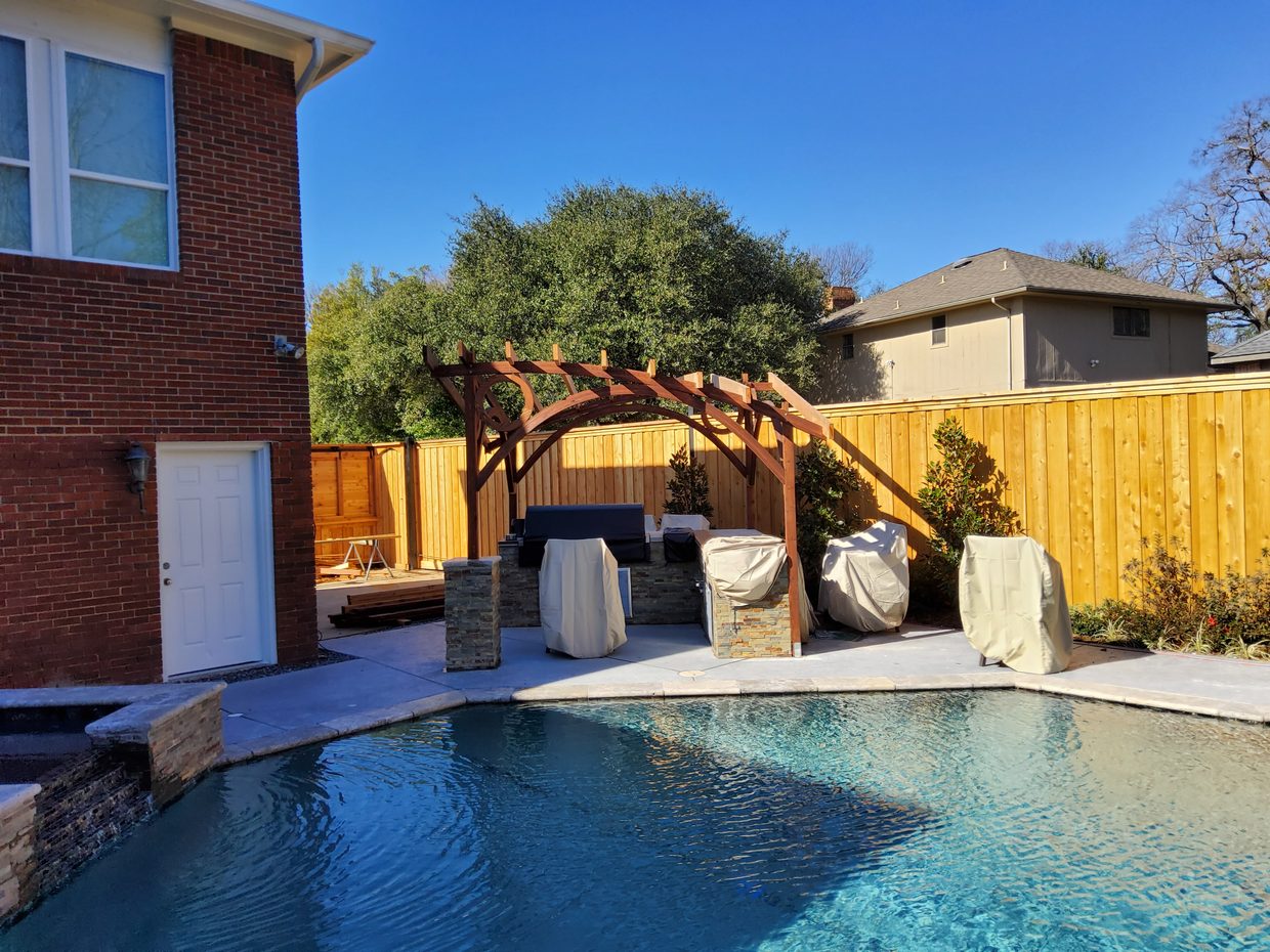 A North Dallas backyard with a cedar fence, an arched pergola, and a pool