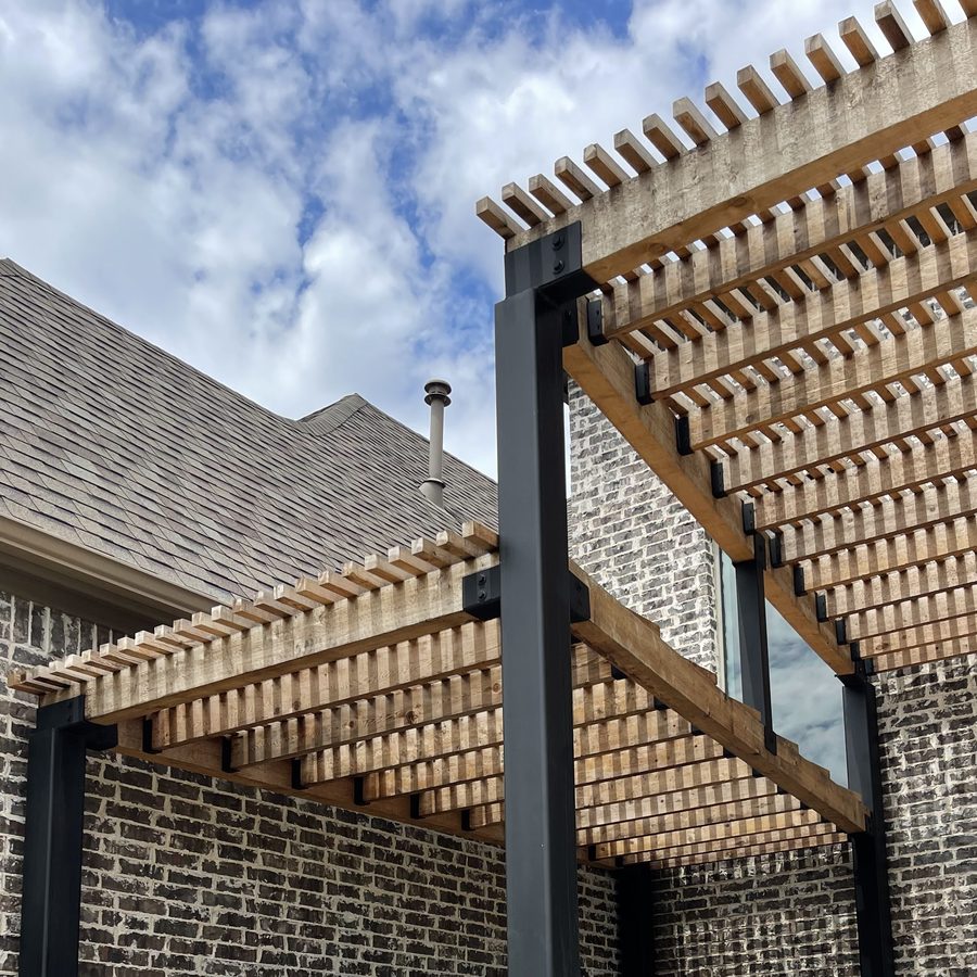 Modern cedar-slat pergola on black steel posts built against a brick North Dallas home