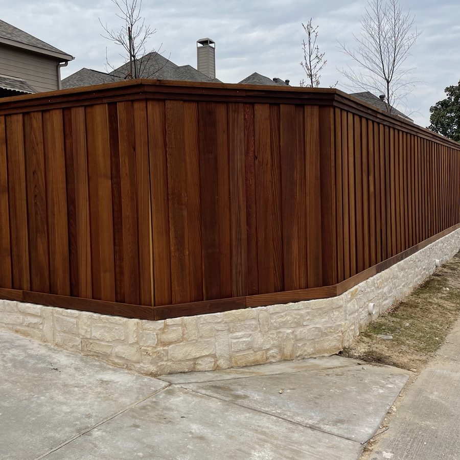 Espresso-stained board-on-board fence with top cap on a cream stone base wrapping a corner lot
